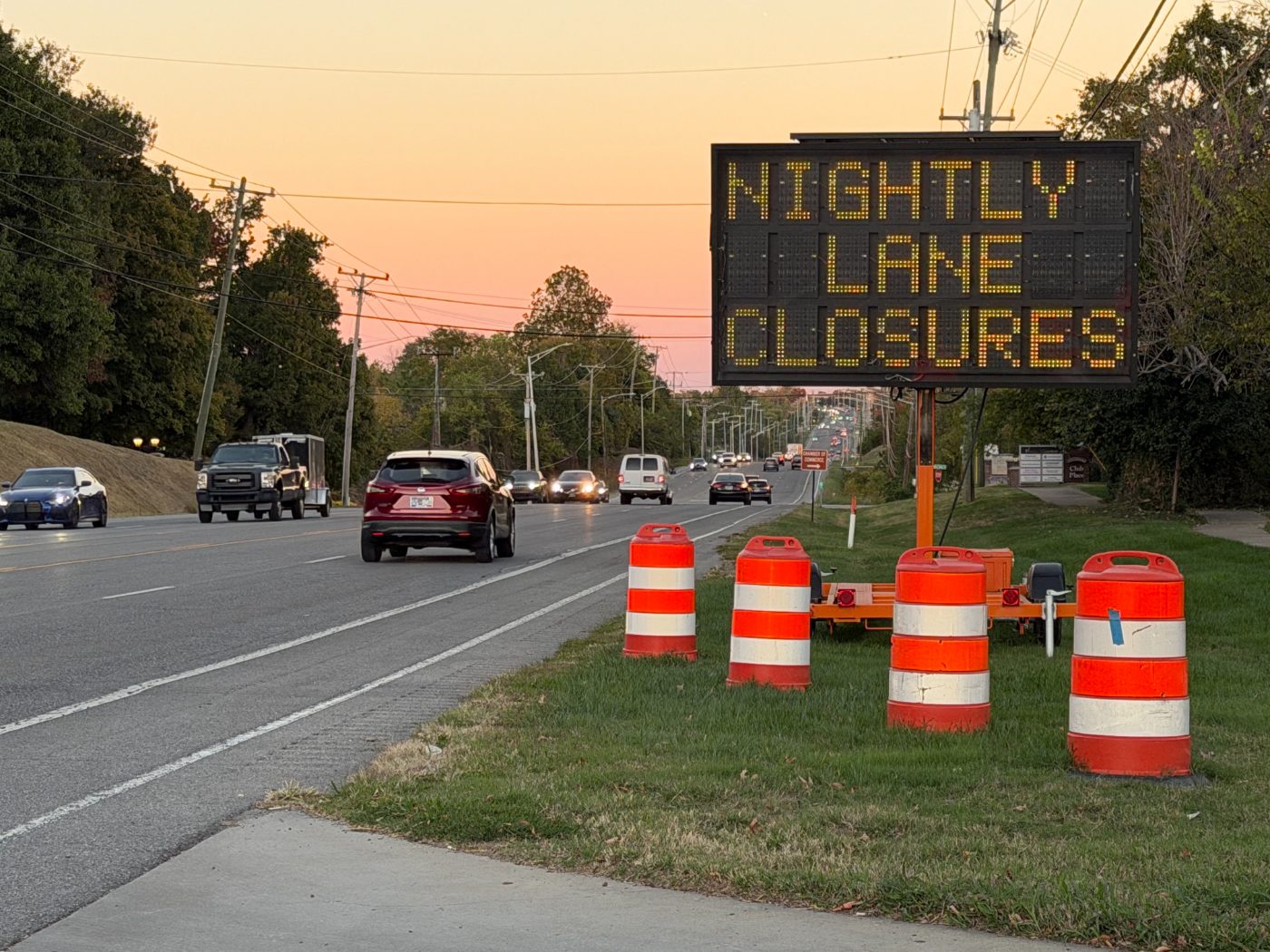 Portable message board reading Nightly Lane Closures beside orange drums along a Middle Tennessee road at sunset