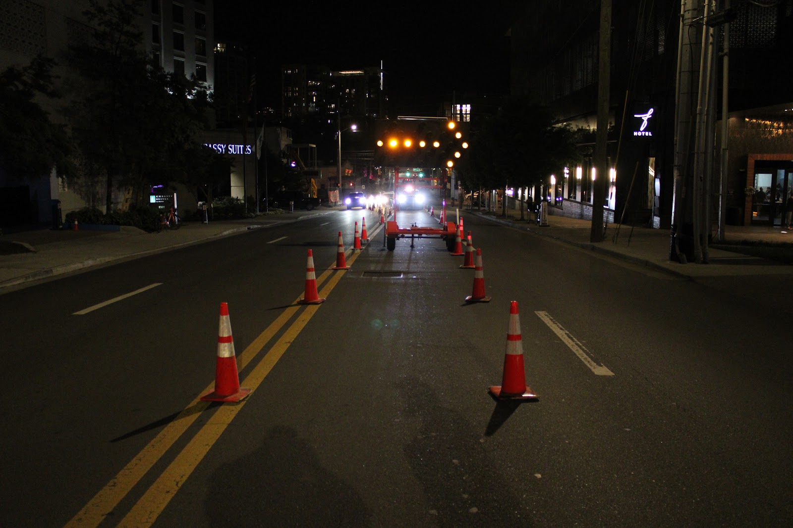Line of channelizing cones closing a lane at night on a Midtown Nashville street with the skyline behind
