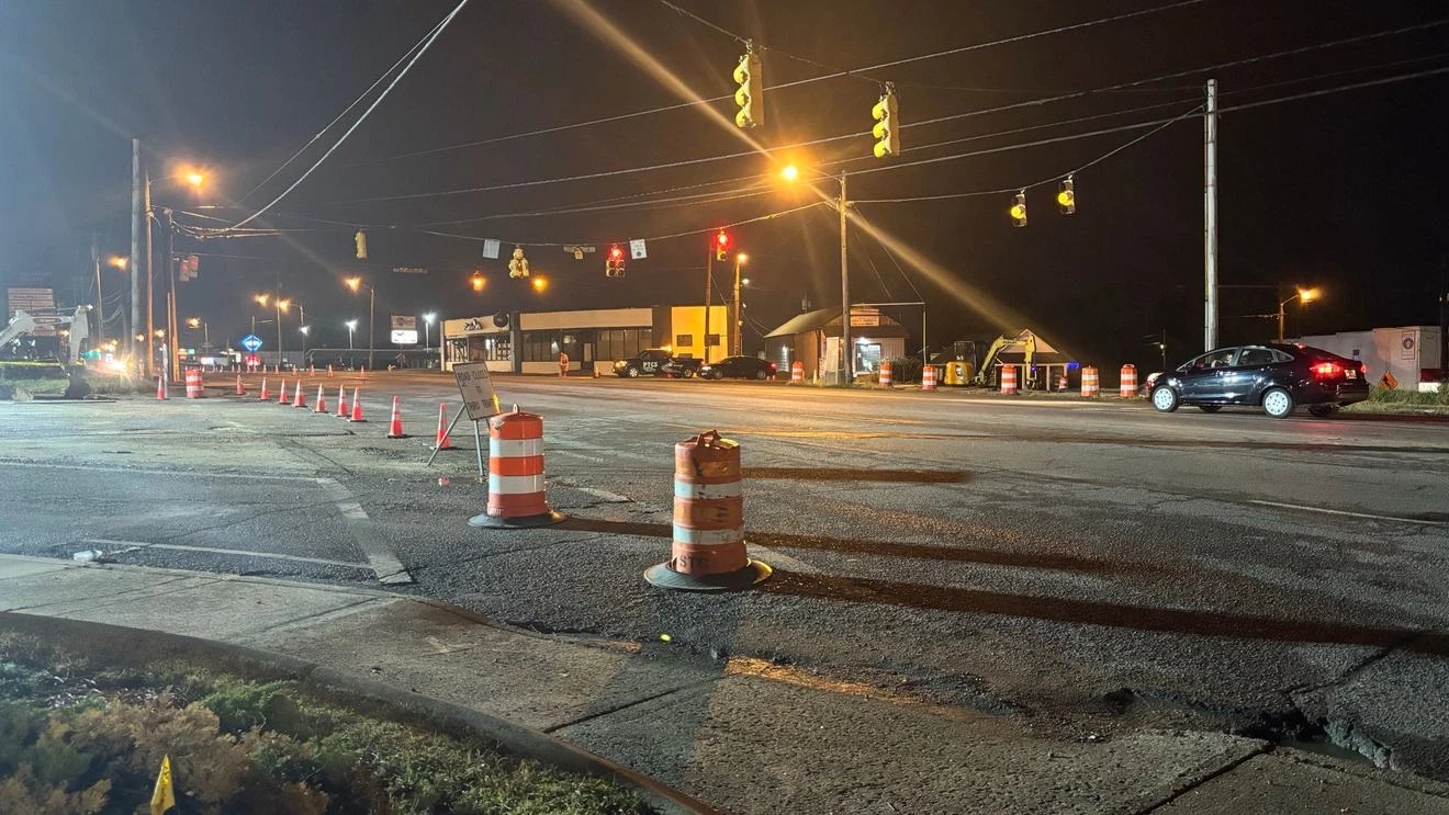 Night road closure at a signalized intersection with orange drums, a line of cones and a Road Closed sign