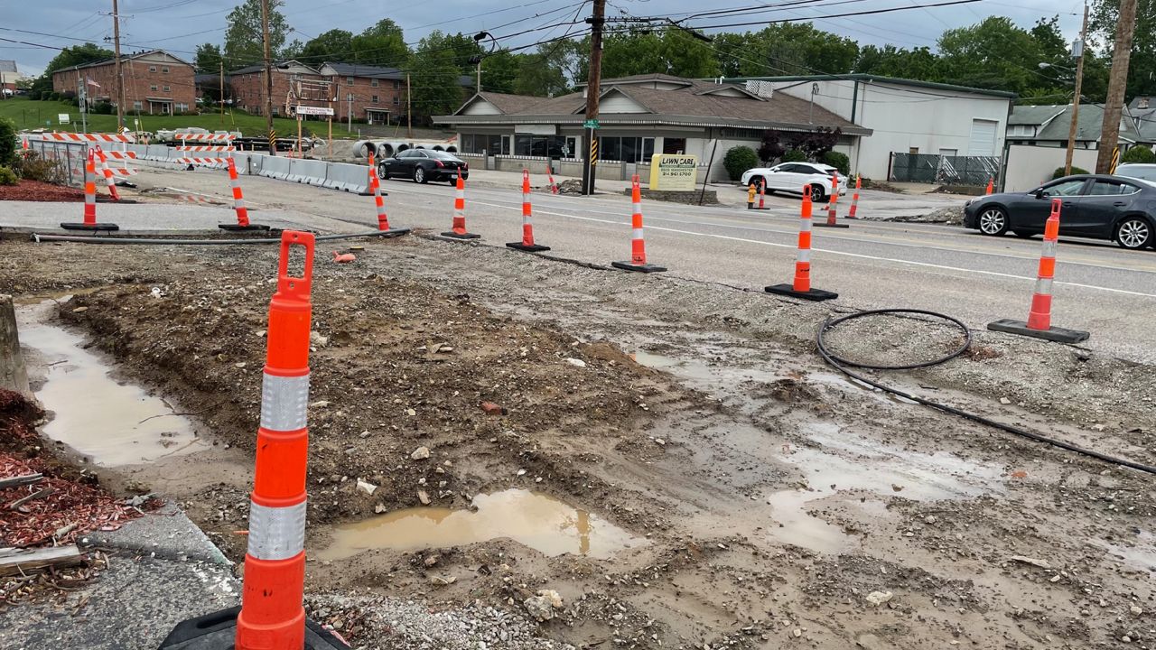 Roadside utility excavation separated from traffic by a line of orange channelizer posts and barrier along a commercial road